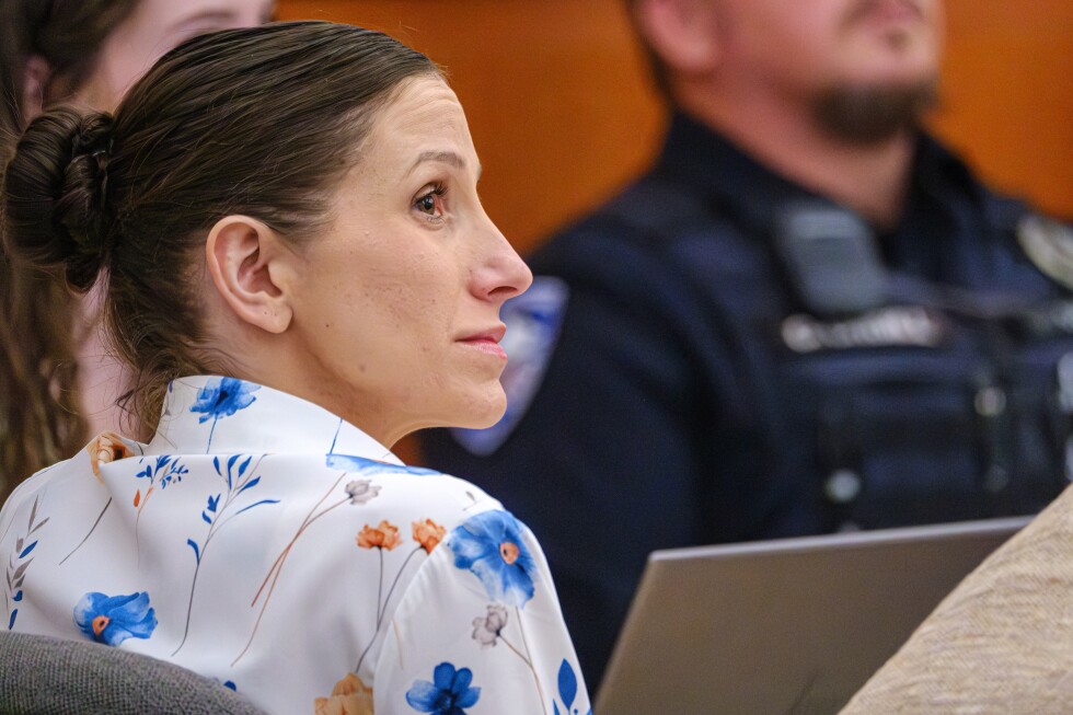 Close-up portrait of woman with dark hair against orange background, appears to be courtroom or media appearance